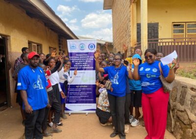 UNIMAC staff in blue T-shirts and students raising their hands beside a banner promoting cultural diversity and tolerance education in the South West, North West and Far North regions of Cameroon