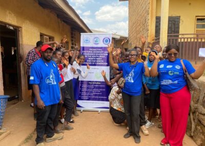 UNIMAC staff and cheering students with raised hands beside a banner promoting cultural diversity and tolerance education in the South West, North West and Far North regions of Cameroon