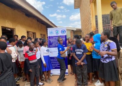 Students gathered around a UNIMAC staff member next to a banner promoting cultural diversity and tolerance education in the South West, North West and Far North regions of Cameroon