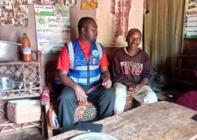A UNIMAC field officer in a reflective vest talking with an elderly man seated in his home