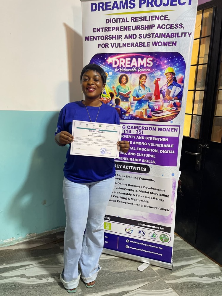 Nsombo Griselda Nvejou smiling and holding her DREAMS Project certificate of participation in front of the project banner