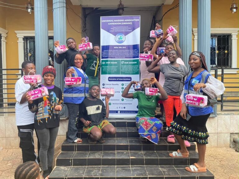 Girls and women holding up sanitary pad packs with UNIMAC volunteers beside the UNIMAC banner